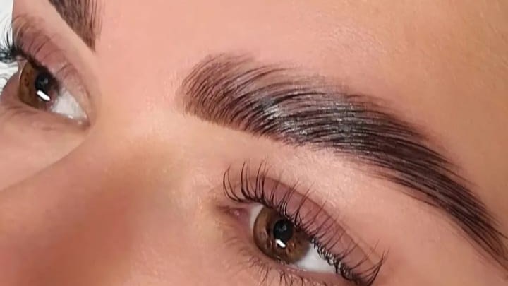 Close-up of a laminated, tinted brow brushed upwards, above lifted lashes