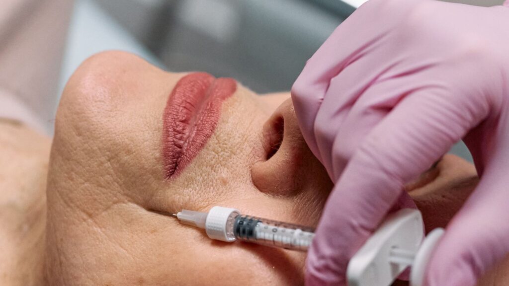 Gloved hand holding a syringe beside a woman's lips