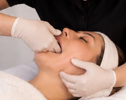 Therapist in gloves massaging a client's cheek from inside and outside the mouth